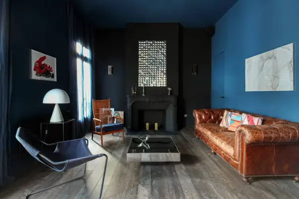 Ein **dunkles Wohnzimmer** mit blau-schwarzen Wänden, Ledersofa, Kamin und moderner Kunst.