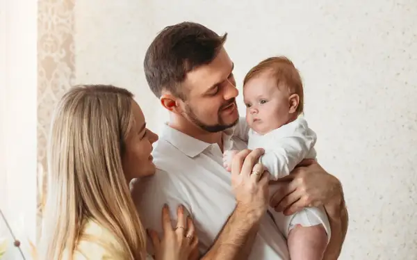 Uśmiechnięta mama i tata patrzą na swoje dziecko, które właśnie zaczyna rozpoznawać twarze.