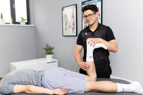 Fizjoterapeuta wykonuje badanie nogi pacjenta leżącego na stole.