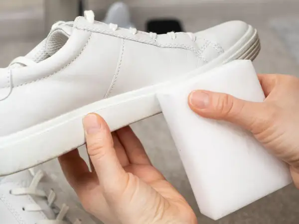 Manos limpiando zapatillas blancas piel con una esponja mágica. ¡Devolviendo el brillo a tus zapatos!