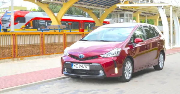 Czerwony Toyota Prius Plus stoi na peronie obok pociągu.