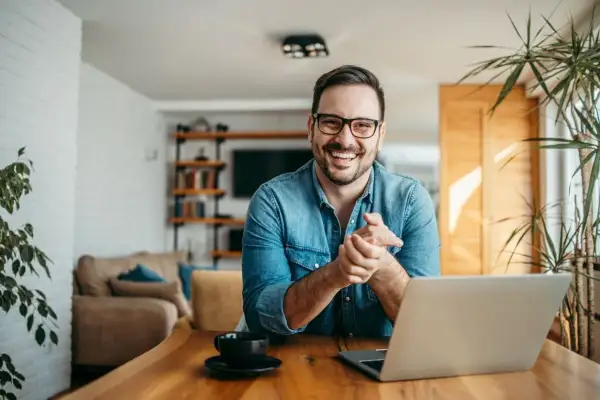 Hombre sonriente con portátil, buscando ideas para negocios rentables en un pueblo.