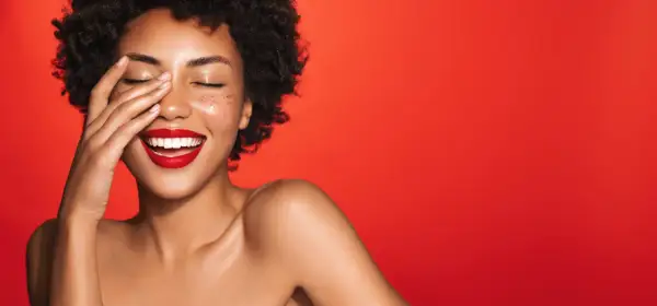 Une femme rit, la main sur le visage, avec un rouge à lèvres éclatant. Quelle couleur de rouge à lèvres !