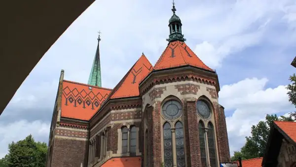 Suchanino kościół z zieloną wieżą i ceglaną fasadą, ozdobiony czerwonymi dachami i ozdobnymi oknami.
