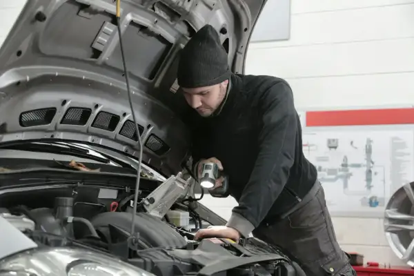 Mechanik bada przyczyny nagłego spadku mocy silnika powyżej 3000 obrotów, oświetlając silnik latarką.