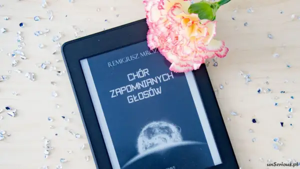 Elektroniczna książka z tytułem "Chór zapomnianych głosów" Remigiusza Mroza, ozdobiona kwiatem i rozsypanymi kryształkami.