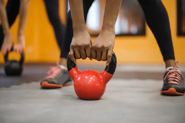 Dłonie zaciskają się na czerwonym kettlebellu. To część treningu fitness, co to za ćwiczenie?