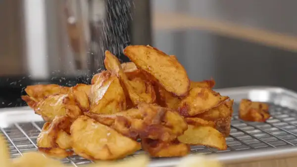 Krispiga potatisklyftor strös med salt efter frityr. Perfekt frityr temp för gyllene, läckra pommes.