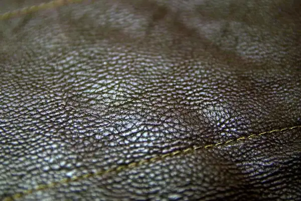 Zbliżenie na fakturę ciemnobrązowej skóry. Real leather to naturalny, trwały materiał, który pięknie się starzeje. Widoczny delikatny szew.