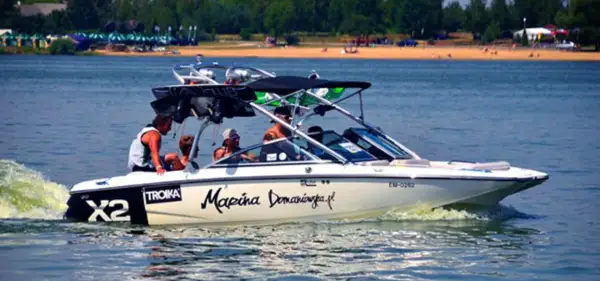 Łódź motorowa z pasażerami płynie po wodzie, tworząc pianę. Na burcie widnieje napis "Marina Domaniewska".