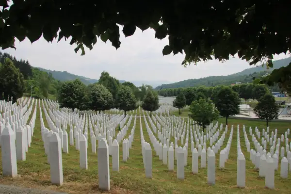 Enormt fält med vita gravstenar, en påminnelse om folkmordet i Srebrenica. Grönskande kullar i bakgrunden.