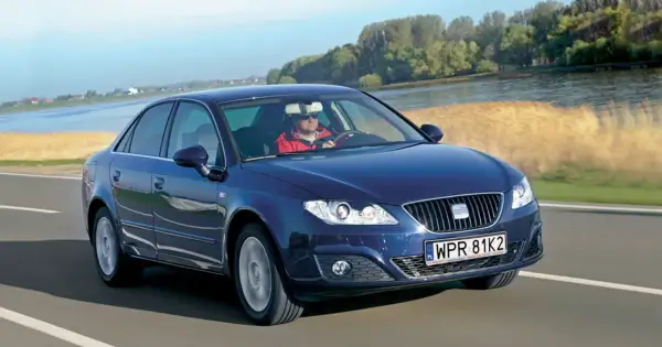 Ciemnoniebieski Seat Exeo 2.0 TDI jedzie drogą nad rzeką, kierowca w czerwonej kurtce.