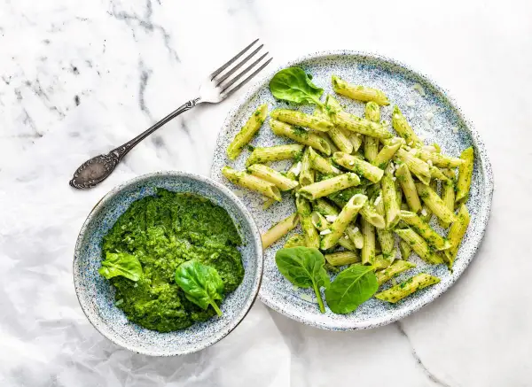 Penne z domowym pesto ze szpinaku, podane w miseczce i na talerzu, z widelcem obok.
