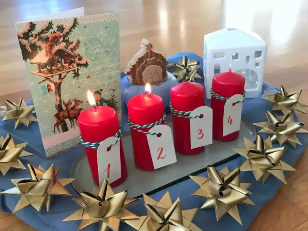 Vier rote Kerzen mit Zahlen 1-4, ein Adventskalender, ein Krippenspiel und goldene Sterne schmücken den Tisch. Perfekt für die Vorfreude auf Weihnachten in der **Advent Grundschule**.