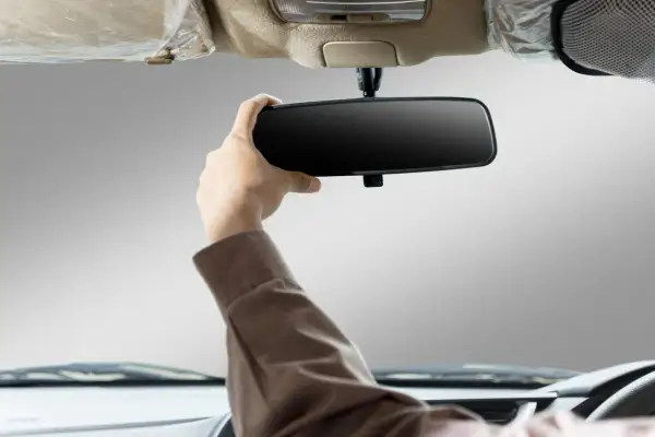 Main d'un conducteur ajustant le rétroviseur intérieur de sa voiture. Apprenez comment emboîter un rétroviseur intérieur pour une meilleure visibilité.