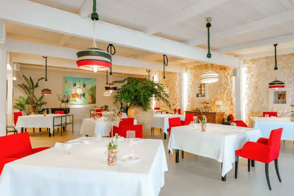 Interni eleganti di ristoranti stellati Puglia, con tavoli apparecchiati, sedie rosse vivaci e un'opera d'arte colorata.