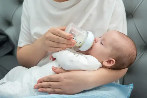 Une main tient un biberon pour nourrir un bébé endormi. La question de savoir si peut on donner de l'eau du robinet à un bébé est importante.