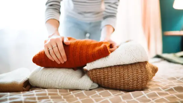 Hände falten warme Pullover. Der Wollprogramm-Waschgang ist abgeschlossen, die Kleidung ist bereit für den Schrank.