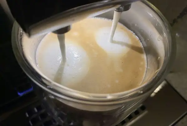 Mleko wylewa się z dyszy ekspresu DeLonghi, tworząc piankę na kawie. Niestety, ekspres DeLonghi nie spienia mleka tak, jak powinien.