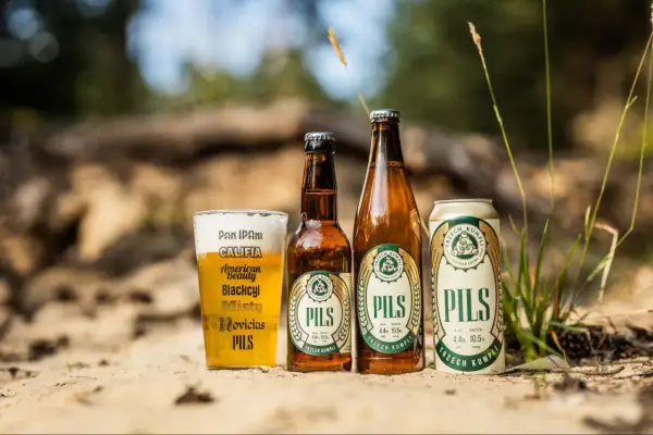 Szklanka i butelki z polskimi piwami typu lager "Pils" od Trzech Kumpli na piasku.