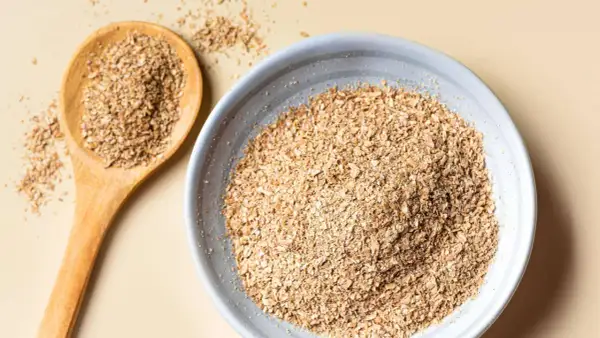Eine Holzschale und ein Löffel gefüllt mit Haferkleie. Haferkleie ist ein nährstoffreiches Nebenprodukt der Haferverarbeitung.