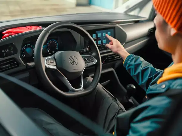 Interni moderni del Volkswagen Caddy: un utente interagisce con il touchscreen centrale, mentre il volante e il cruscotto digitale sono ben visibili.