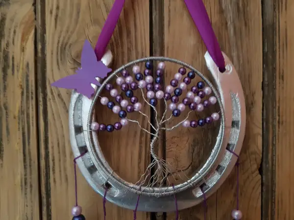 Tuto attrape rêve arbre de vie : un fer à cheval argenté orné d'un arbre de vie en fil de fer et perles violettes et roses, avec un papillon violet.