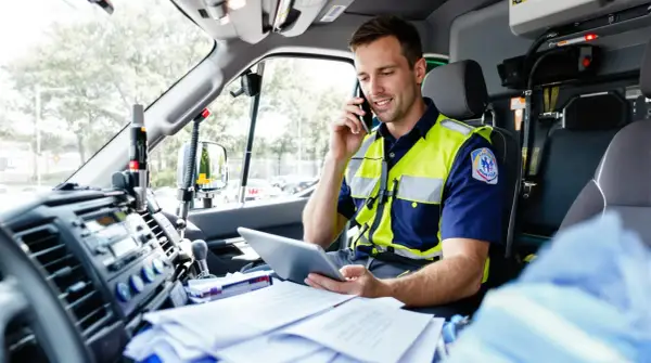 Paramédic en uniforme, parlant au téléphone et consultant une tablette dans un véhicule prioritaire, respectant le code de la route.