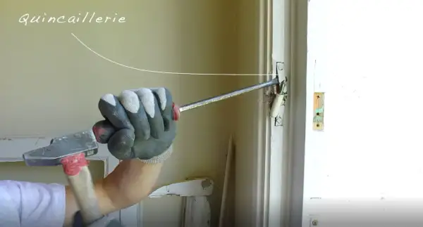 Main tenant utilise un marteau pour ajuster la quincaillerie d'une porte, travaillant sur une pose en feuillure.