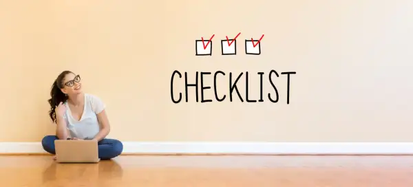 Młoda kobieta z laptopem siedzi na podłodze. Na ścianie nad nią widnieje napis "CHECKLIST" z trzema zaznaczonymi polami.