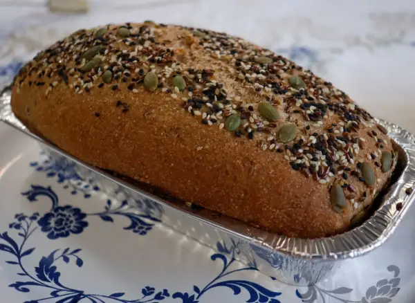 Chleb Ezechiela w formie bochenka, posypany pestkami dyni, sezamem i siemieniem lnianym, w aluminiowej foremce.