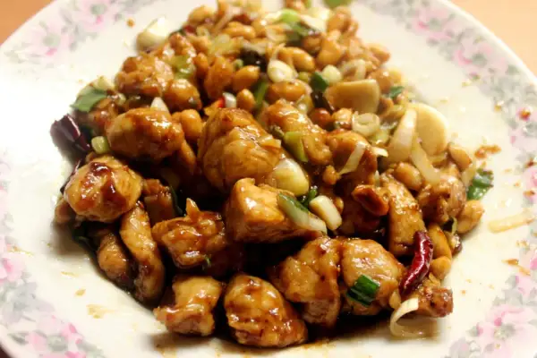 Kurczak Gong Bao z orzeszkami ziemnymi, cebulą i papryczkami chili na talerzu.