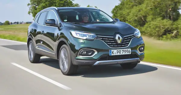 Zielony Renault Kadjar jedzie po drodze, za kierownicą mężczyzna w okularach.