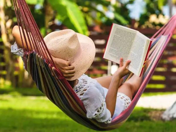 Une personne lit un livre dans un hamac coloré, profitant d'un des 7 types de repos sous un chapeau de paille.