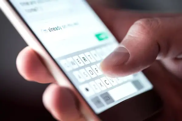 Palec pisze na klawiaturze telefonu: "Już w drodze". Potwierdzenie przybycia na wesele sms.