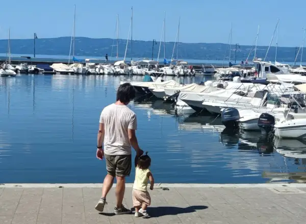 Padre e figlia passeggiano sul lungolago di Bolsena, con barche ormeggiate sullo sfondo.