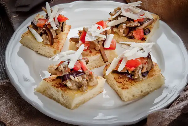 Deliziosi crostini con melanzane, pomodoro e scaglie di formaggio su pane tostato.