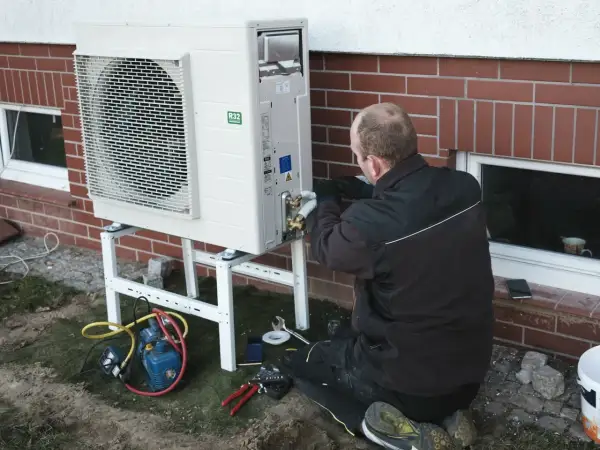 Instalator pracuje nad pompą ciepła, zapewniając jej ekonomiczne ustawienie. Widać narzędzia i sprzęt do montażu.