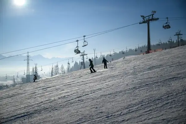 Narciarze i snowboardziści szusują po ośnieżonym stoku, podziwiając piękne widoki. Białka Tatrzańska oferuje wspaniałe atrakcje zimą.