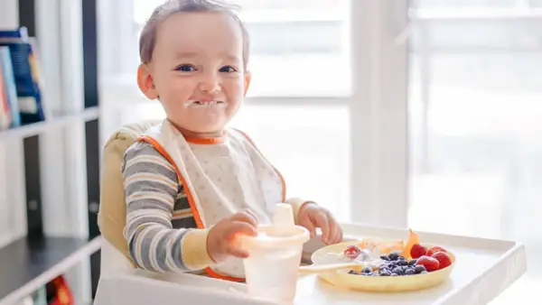 Kleiner Junge mit Heidelbeeren und Joghurt im Gesicht, der an seinem Becher nippt.