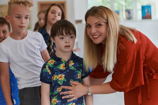 Eine Frau in Rot lächelt und legt ihre Hand auf die Schulter eines Jungen mit Down-Syndrom. Man darf behindert sagen, wenn man über Inklusion spricht.