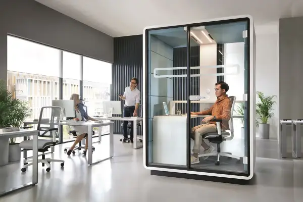 Bureau moderne avec un espace ouvert, une cabine vitrée pour des appels privés et des postes de travail.
