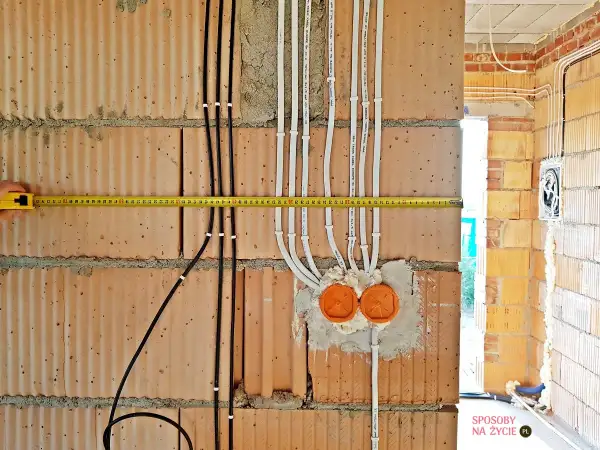 Instalacja elektryczna w domu w trakcie budowy. Widoczne przewody, puszki i miarka.
