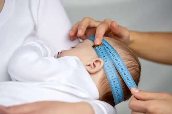 Dziecko mierzone centymetrem. Wynik można porównać z obwód główki niemowlaka tabelą.