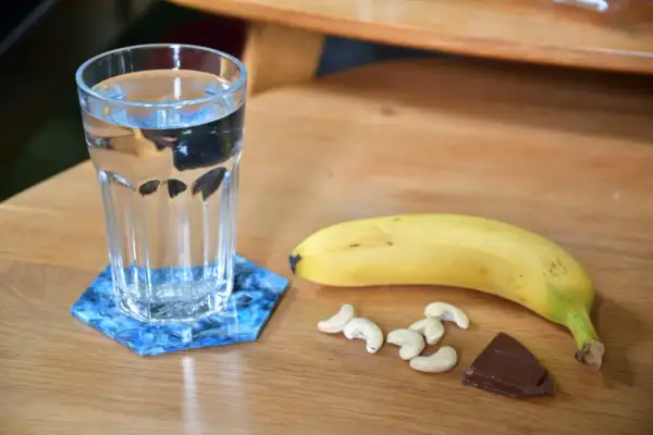 Verre d'eau, banane, noix de cajou et chocolat : idéal pour savoir quoi manger avant de courir le matin.