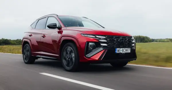Czerwony Hyundai Tucson 1.6 T-GDI N Line pędzi po drodze, otoczony zielonymi polami i drzewami.