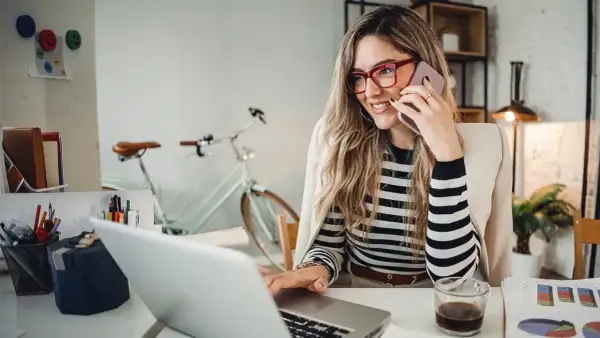 Frau am Telefon, lächelnd, am Laptop arbeitend. Hinter ihr ein Fahrrad. Perfekt für den **iu semesterbeginn**-Stress.