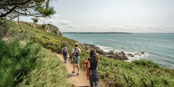 Trois randonneurs explorent un sentier côtier verdoyant, le **gr 34**, face à la mer d'un bleu profond.