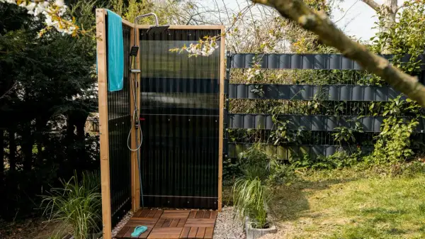 Doccia da giardino fai da te con pedana in legno, telo azzurro e rubinetto. Perfetta per rinfrescarsi all'aperto.