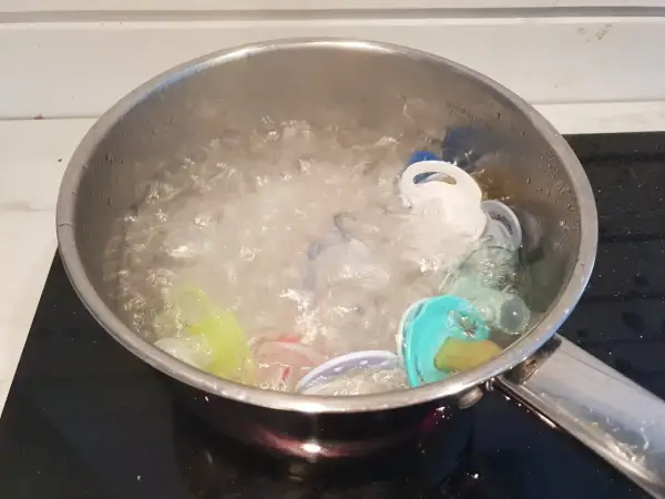 Flera nappar i olika färger kokas i en kastrull med bubblande vatten för att desinficera dem.
